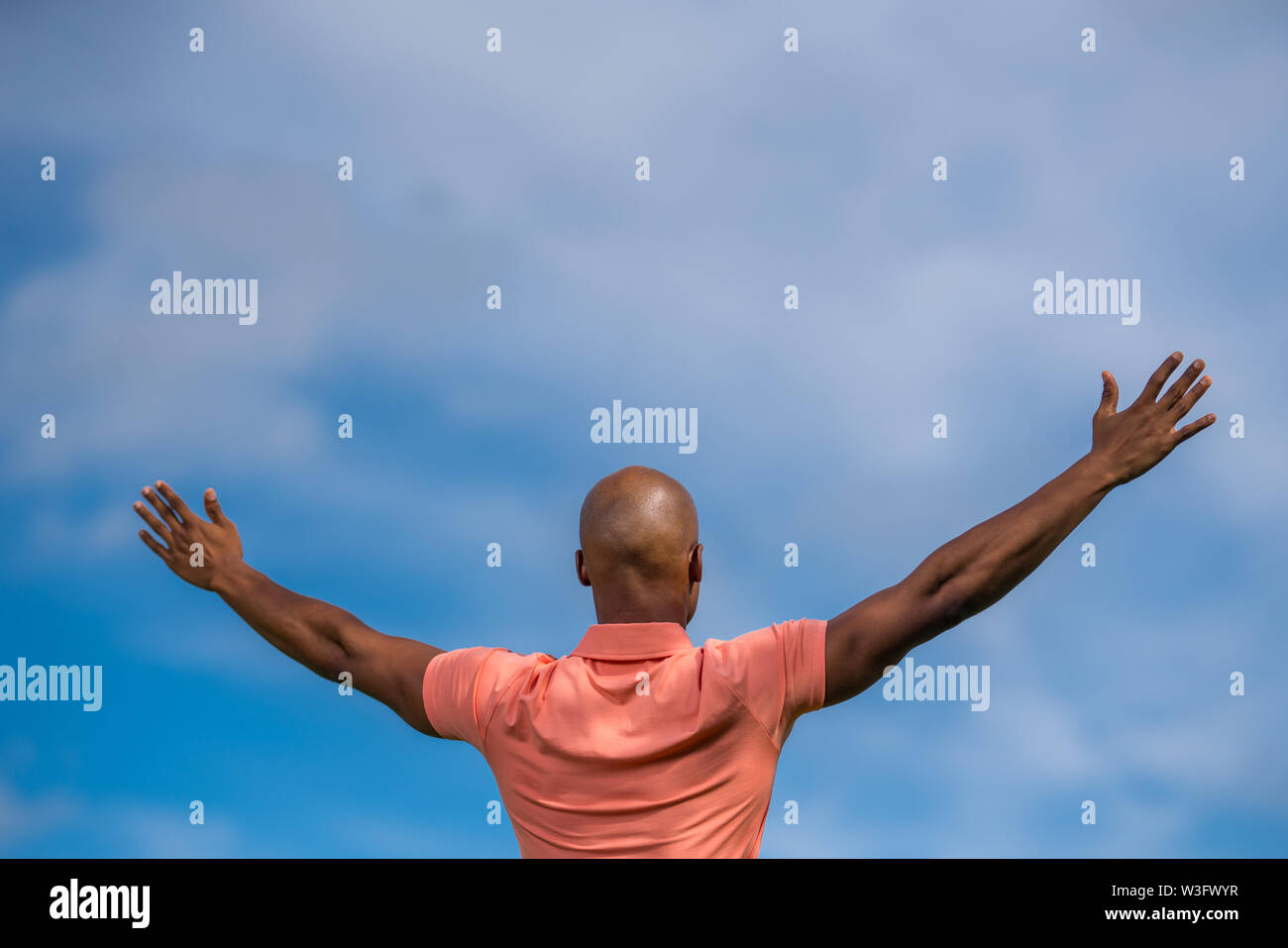Portrait of a African American man facing away from the camera with arms open towards blue sky Stock Photo