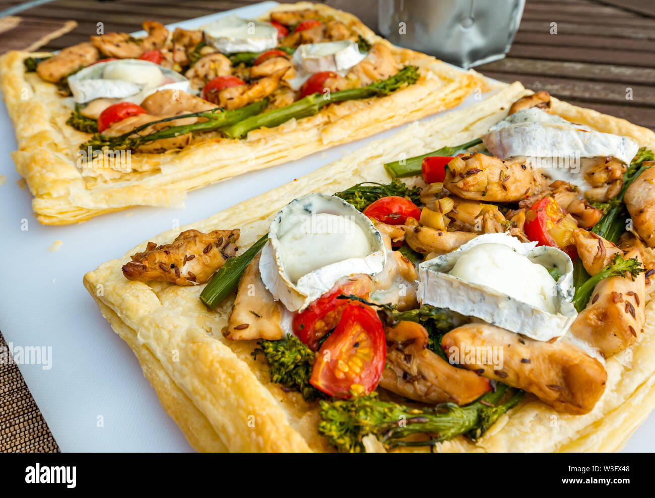 Summer food: meal served outdoors with goat's cheese, broccoli, tomatoes and chicken on puff pastry slices Stock Photo