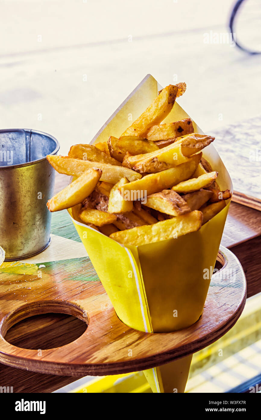 French Fries potato in a yellow paper bag, ready to eat, cutted sliced putted in a wooden holder in a dutch cafe. Holland Stock Photo