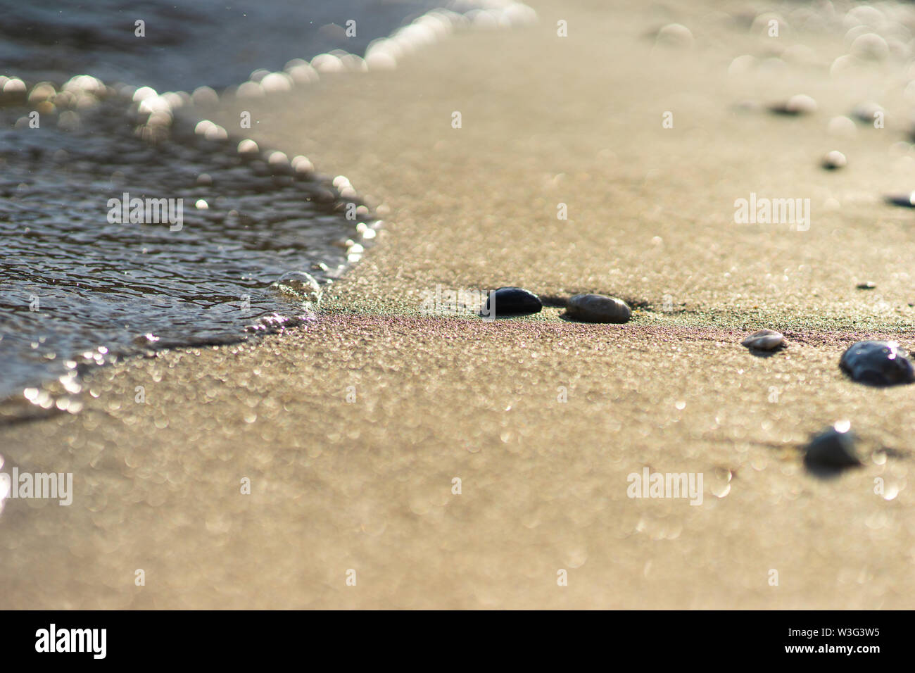close up of a sandy beach with small pebbles and a wave coming in Stock Photo