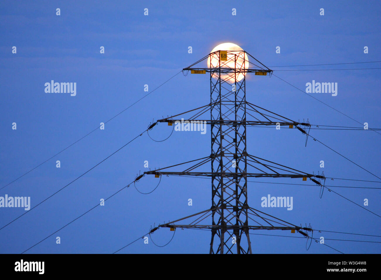 Power line pylon with a full moon in the background Stock Photo
