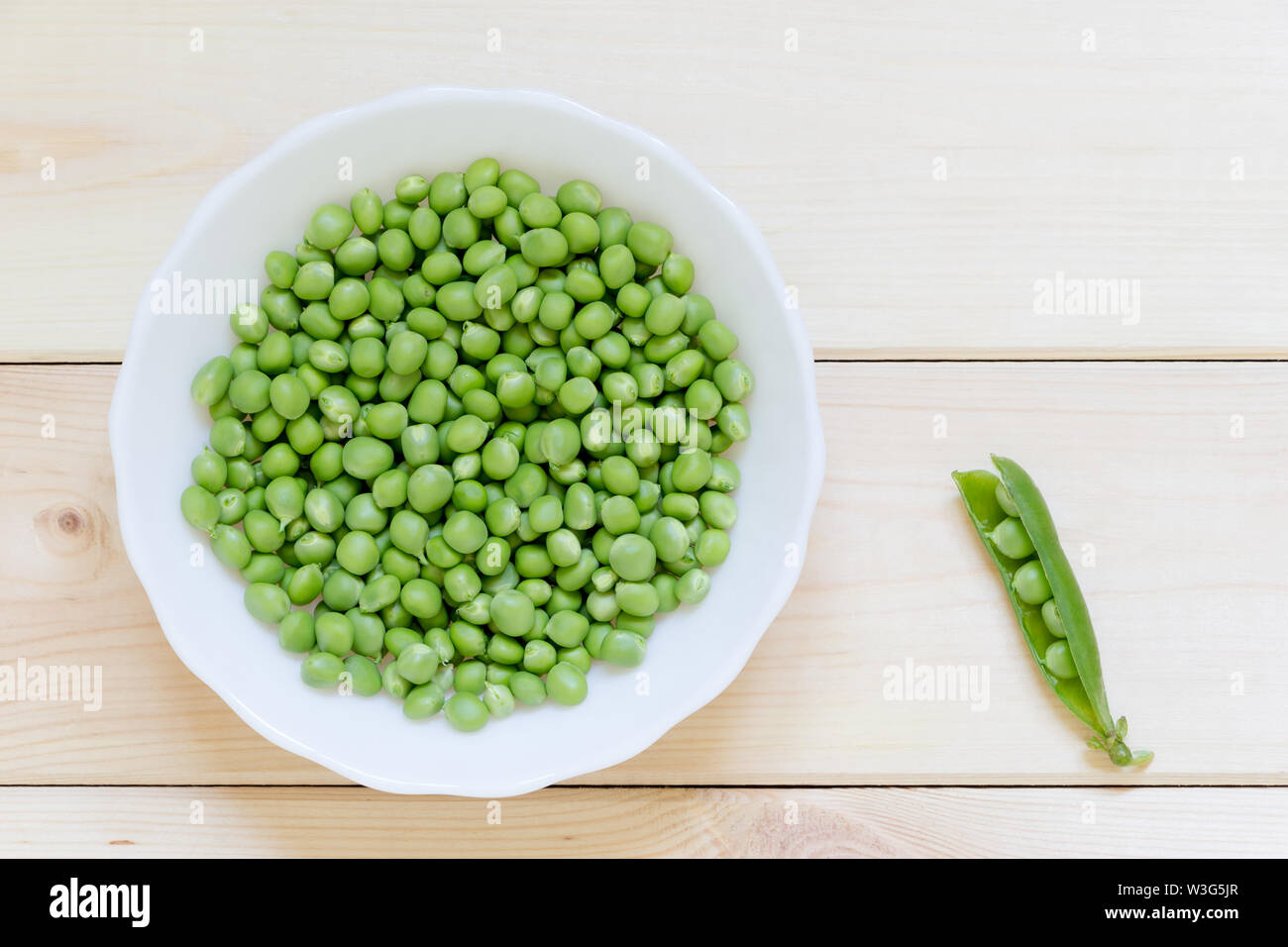 Green peas ready to eat on white plate on light wooden table with copy space. Top view. Single open pod. Delicious fresh home-grown vegetables. Health Stock Photo