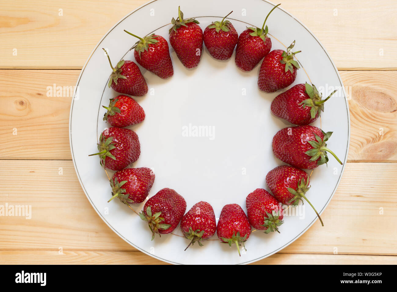 Red ripened strawberries laid out in circle shape on white plate on light wooden table. Copy space in center of frame. Place for text. Delicious natur Stock Photo