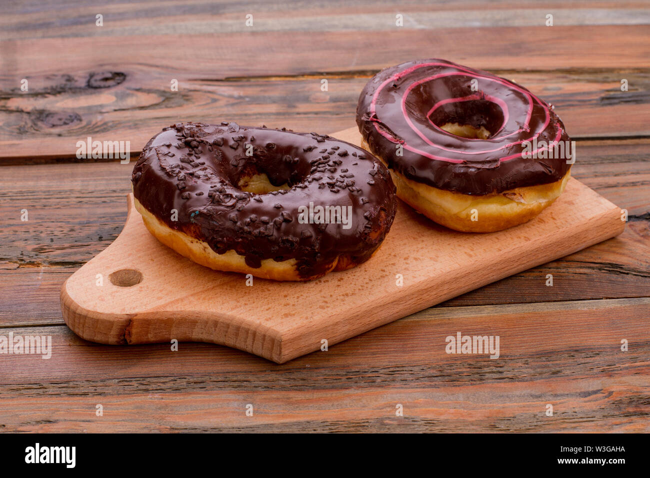 Two chocolate donuts on cutting board. Stock Photo