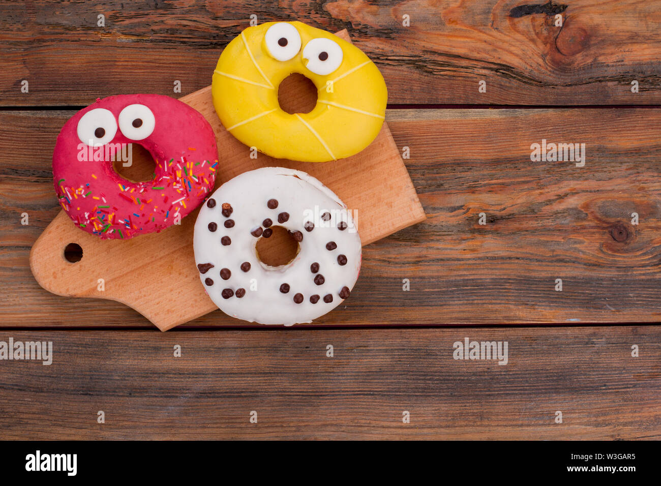 Funny decorated donuts on wooden background. Stock Photo