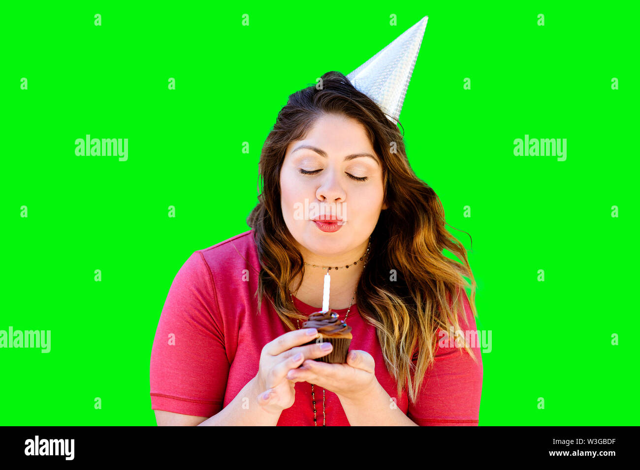 Woman blowing out her birthday candle on a chocolate cupcake on green screen Stock Photo