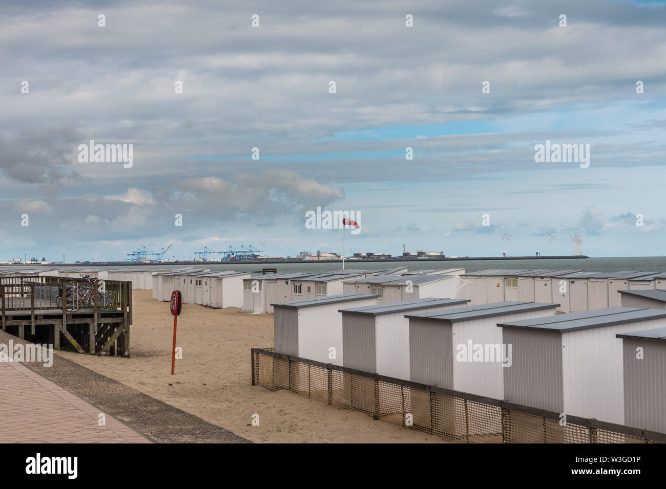 Knokke-Heist, Flanders, Belgium -  June 16, 2019: Knokke-Zoute part of town. Rows of white beach cabins on the sand with Zeebrugge LNG-sea terminal in Stock Photo