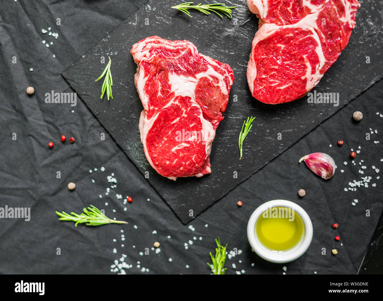 Rib eye beef cow steak meat with spices and herbs against black
