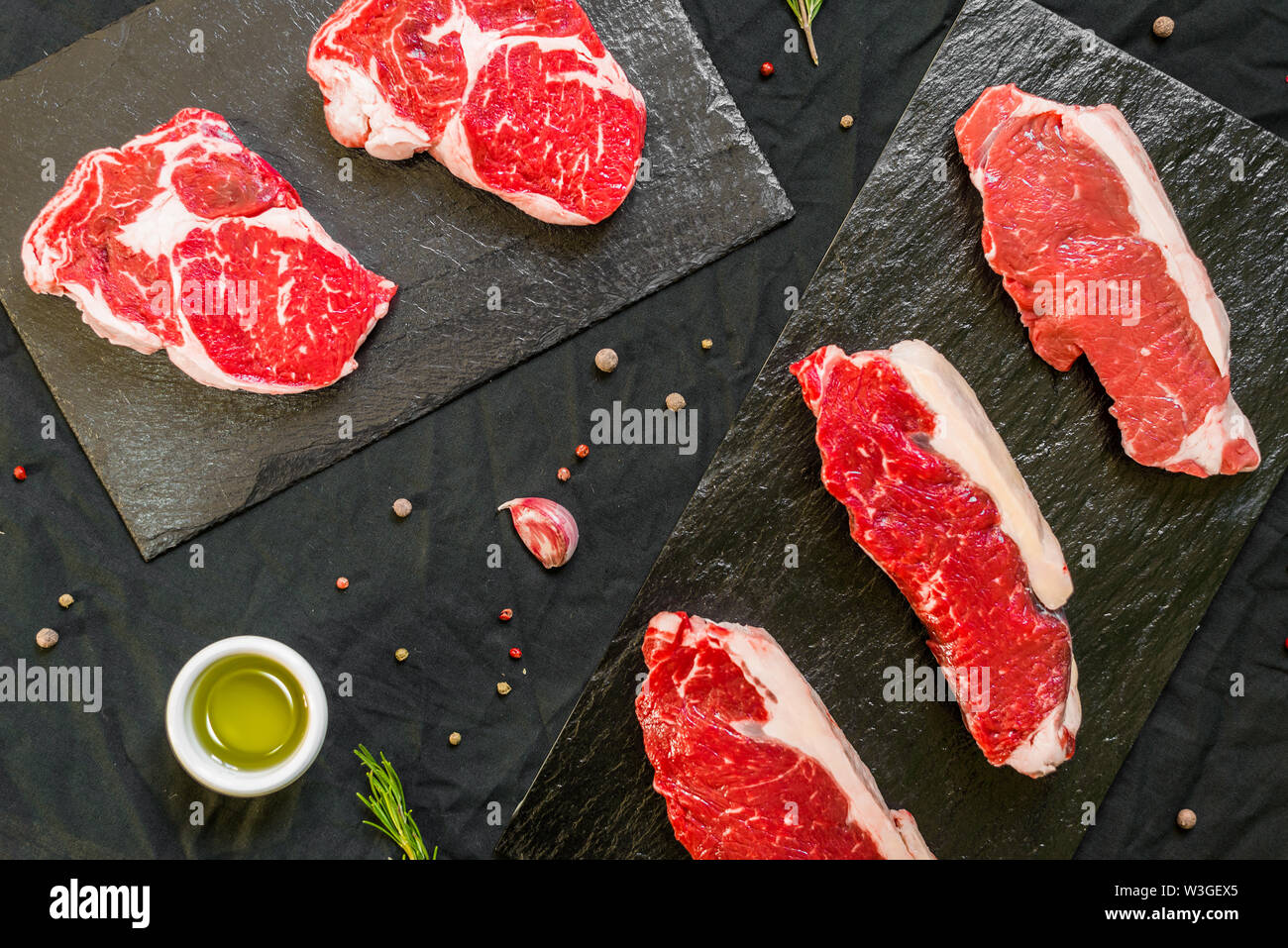 Beef cow meat steaks with spices and herbs against black background Stock Photo