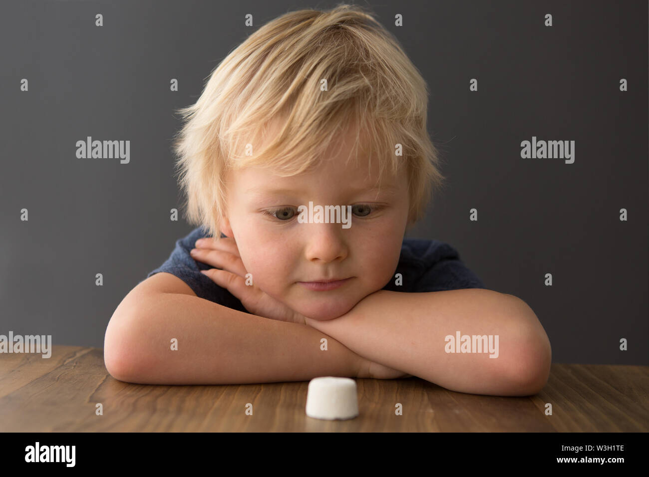A young boy sits at a table with a single marshmallow, attempting the