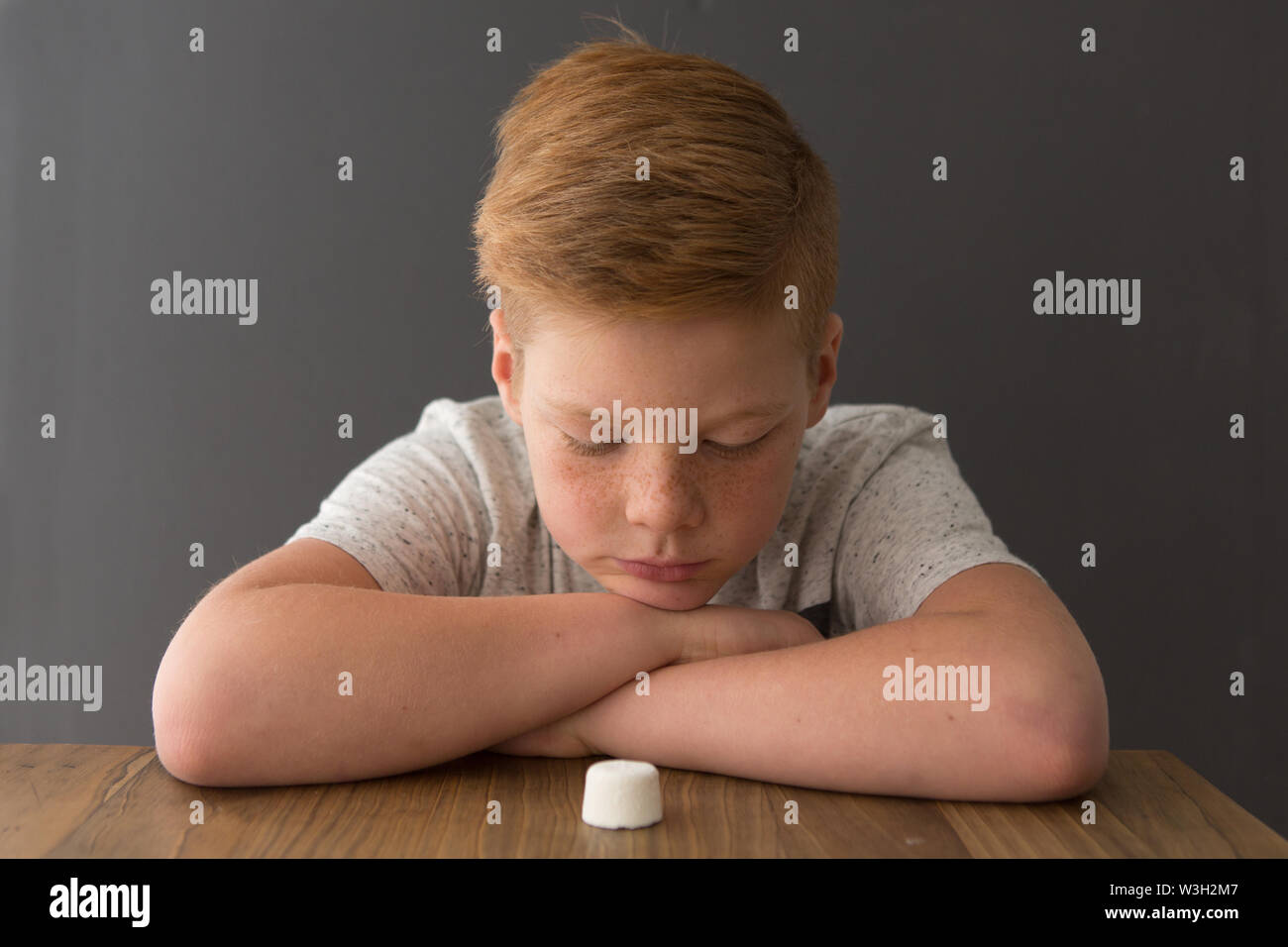 Red-head caucasian boy sits at a table with a single marshmallow, attempting the marshmallow test Stock Photo