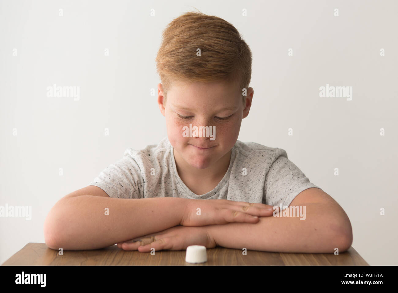 Red-head caucasian boy sits at a table with a single marshmallow, attempting the marshmallow test Stock Photo