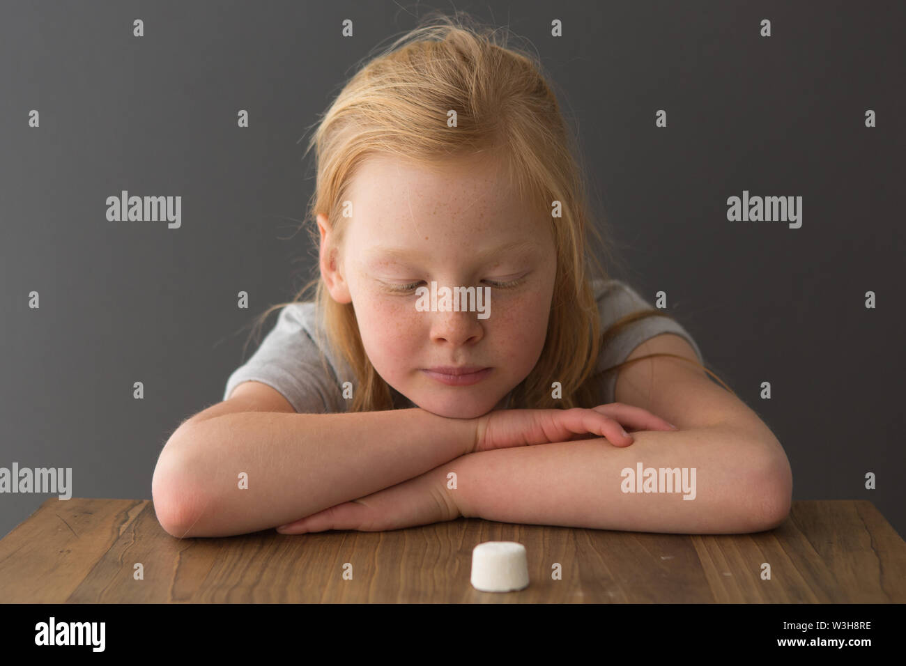 A young girl looks at a single marshmallow, attempting the marshmallow test Stock Photo