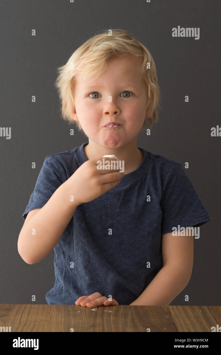 A young boy sits at a table eating a marshmallow, failing the marshmallow test Stock Photo Alamy