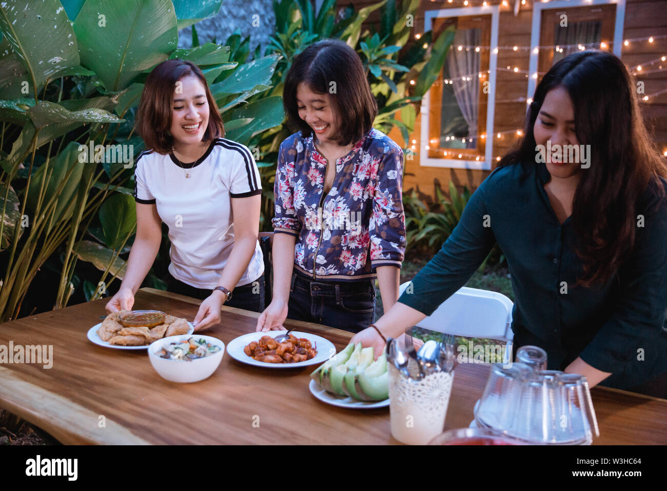 three woman preparing table for dinner at home backyard garden party ...