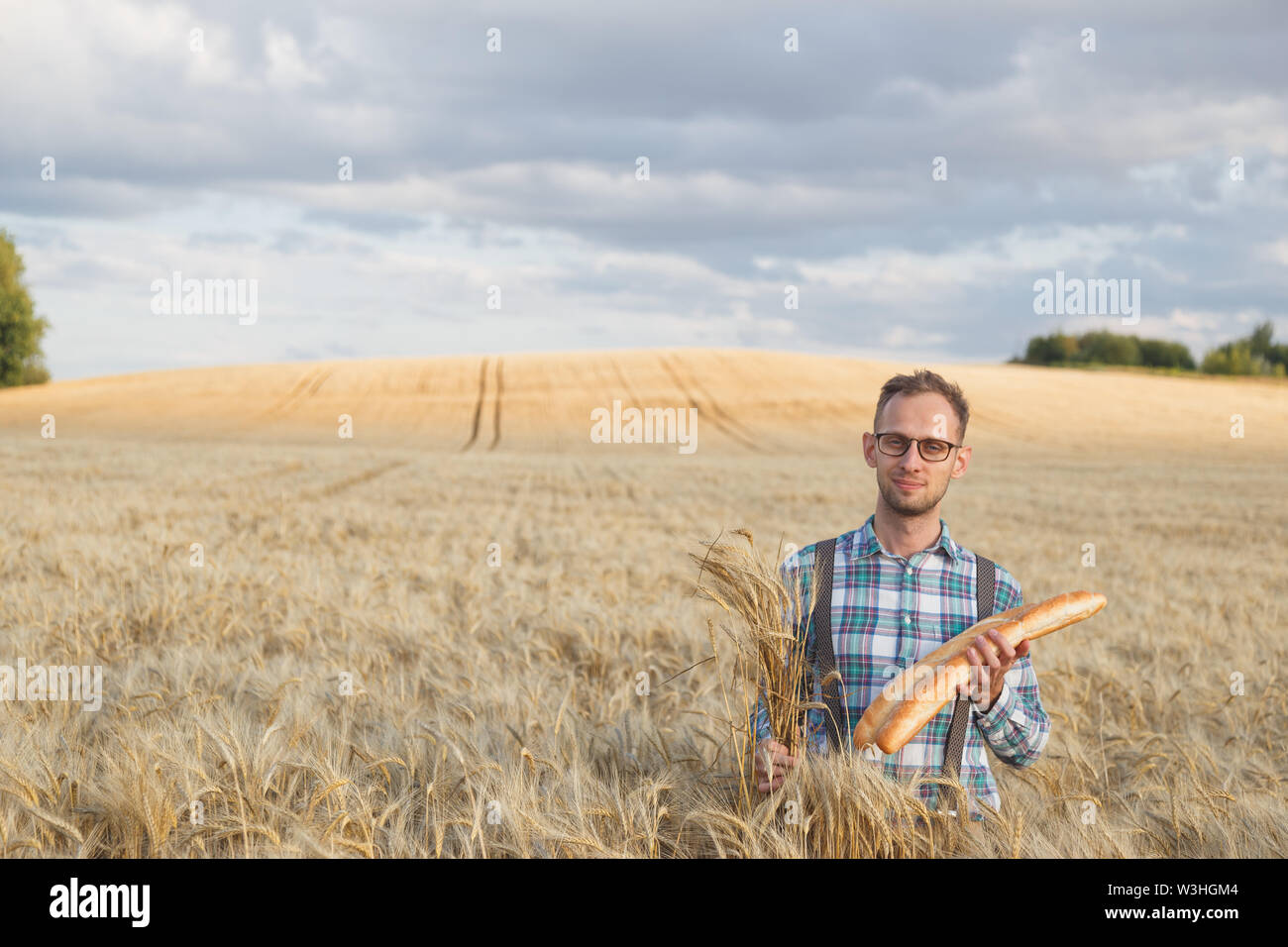 Happy farmer hold bakery products and ears of corn standing in ripe ...