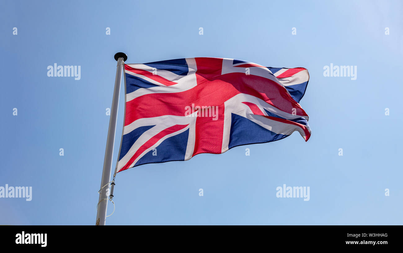 United Kingdom flag, Great Britain national symbol waving against clear blue sky, sunny day Stock Photo