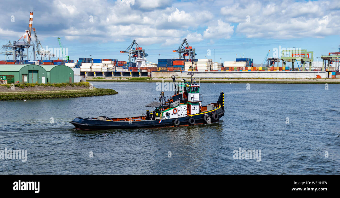 Tug boat, containers and huge cranes at international harbor of Rotterdam, Netherlands, sunny day. Logistics business. Stock Photo