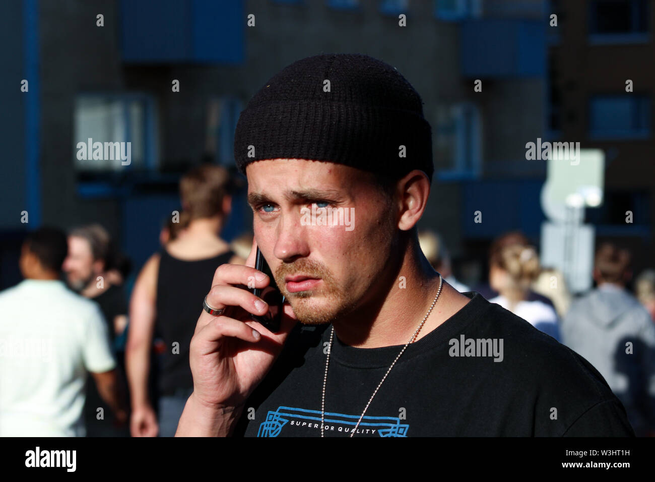 Man wearing knit cap speaking on phone in the street during Kallio Block Party 2017 in Helsinki, Finland Stock Photo