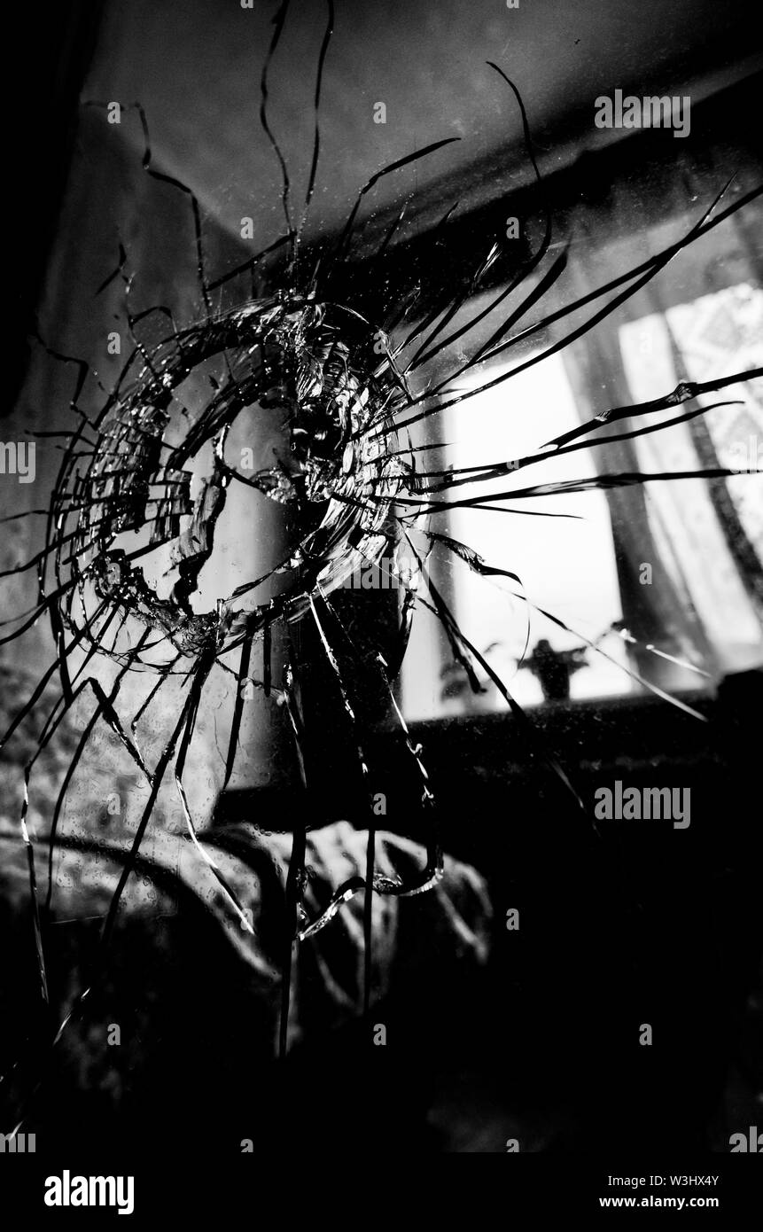 Broken glass with cracks and a hole stylized black and white film and lomography in the background of the window in the room Stock Photo