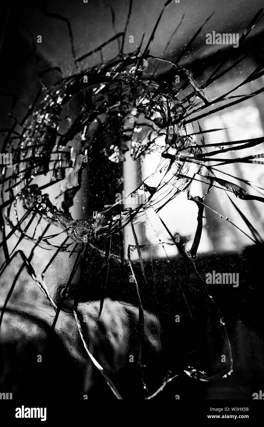 Broken glass with cracks and a hole stylized black and white film in the background of the blurred room closeup Stock Photo
