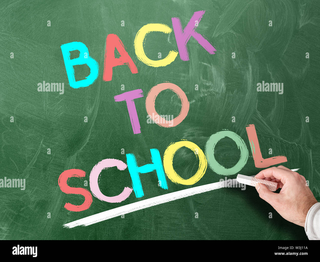 hand holding piece of chalk against colorful words BACK TO SCHOOL written on chalkboard Stock Photo