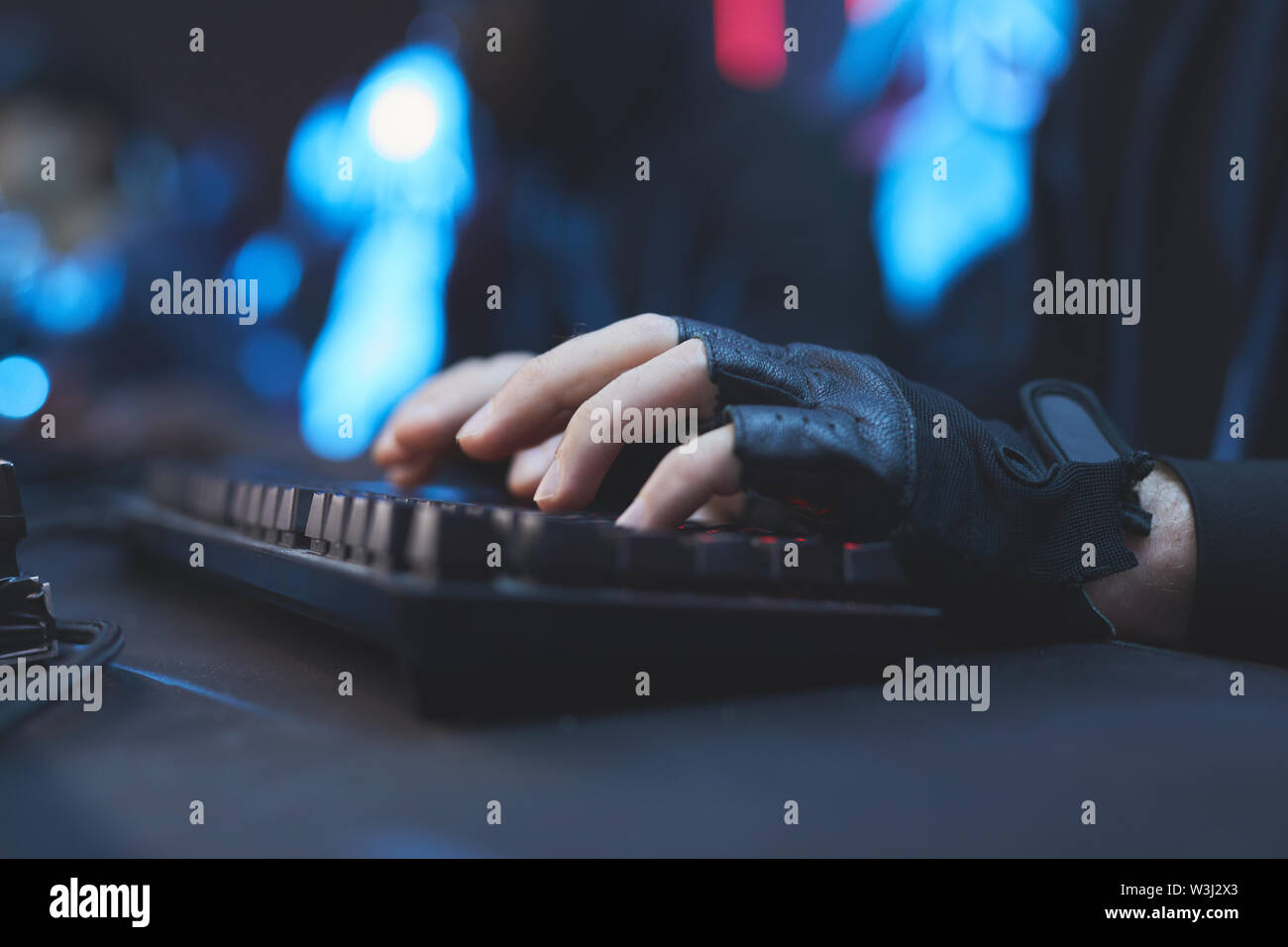 Close-up of unrecognizable hacker in black fingerless gloves sitting at desk and typing on computer keyboard while working on virus Stock Photo