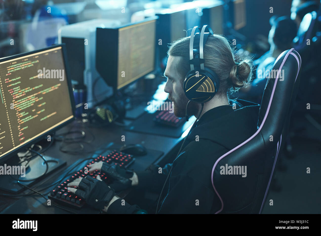 Serious concentrated bearded web developer with beard and ponytail sitting at table and coding app Stock Photo