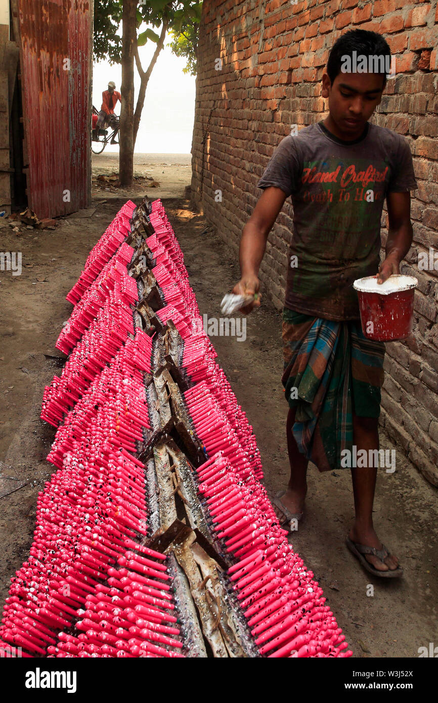A labourer colours racks of rubber balloon in the sun as he works at a balloon factory in Dhaka, Bangladesh. Stock Photo