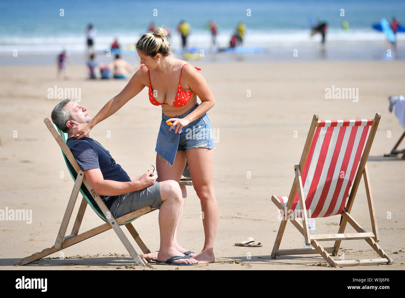 Sunbathers apply sunscreen during the hot sunshine on Towan beach in Newquay, Cornwall, the week before school holidays, as more hot weather is due to hit the UK this week. Stock Photo