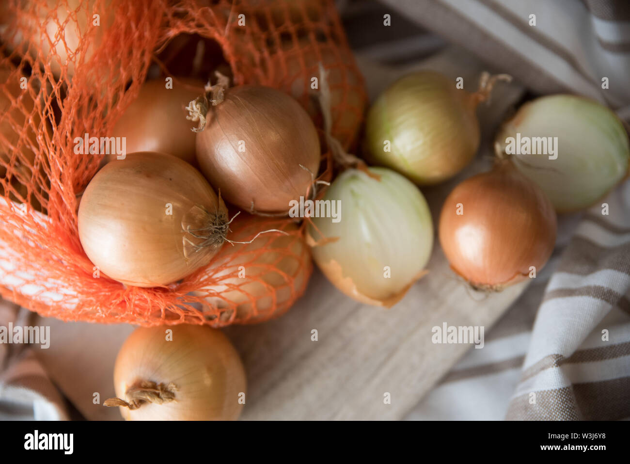 Yellow onions on a wooden cutting board atop a table with tablecloth Stock Photo