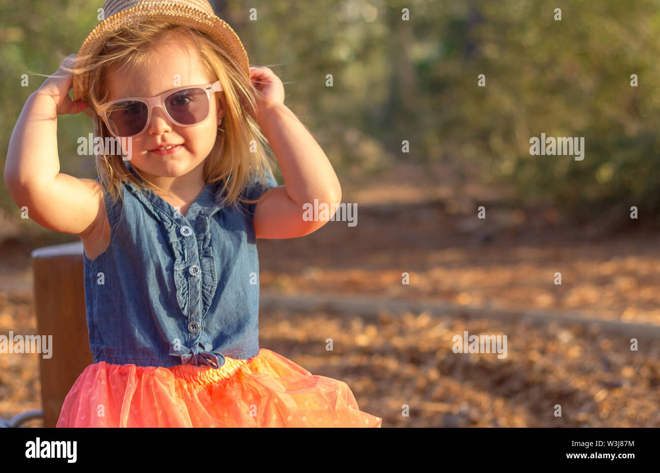 A cute blonde little girl in the park. She is wearing a hat and sunglasses Stock Photo