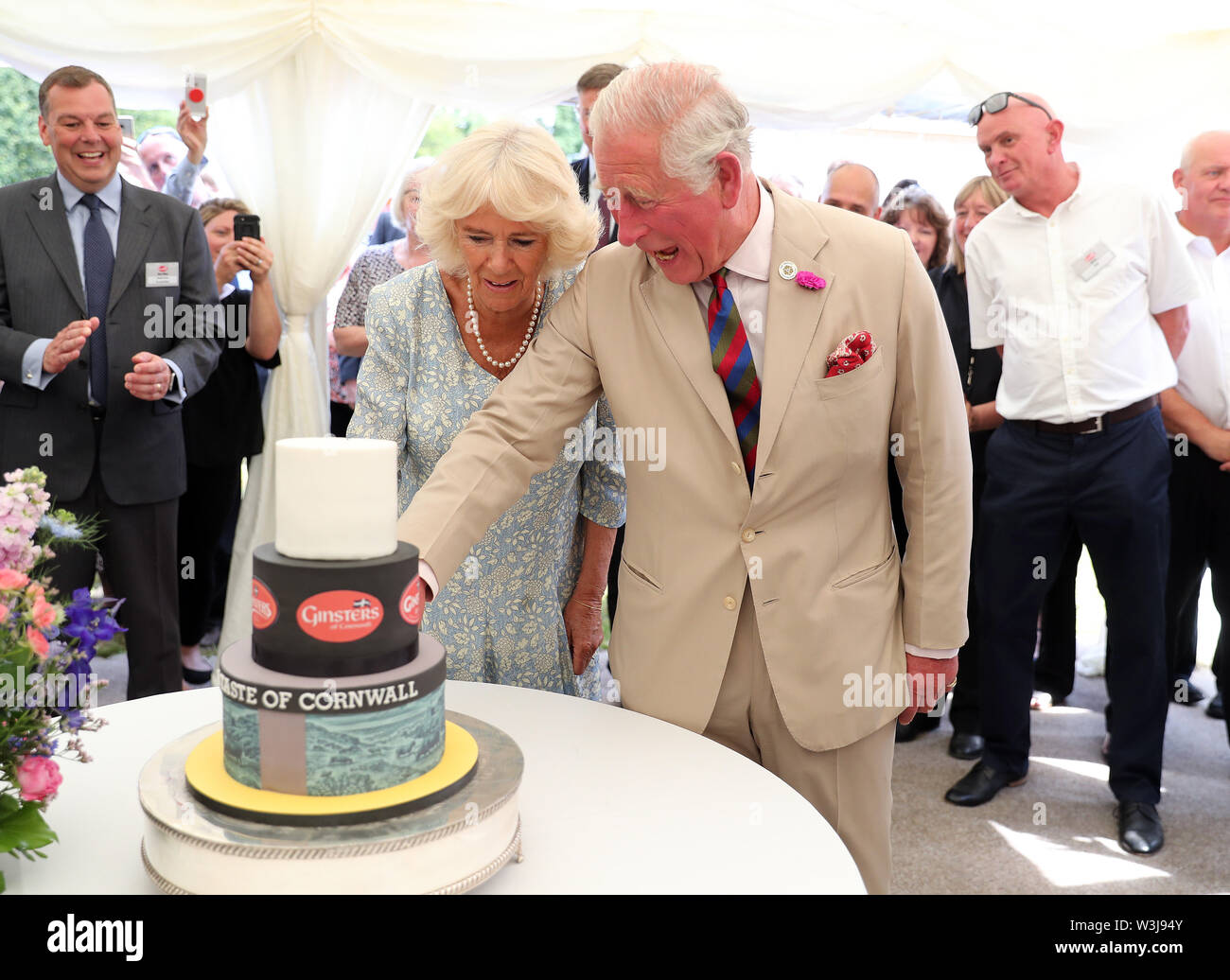 The Prince of Wales and the Duchess of Cornwall cut a cake during a garden party to celebrate the 50th anniversary of Ginsters bakery in Callington, as part of their visit to Cornwall. Stock Photo