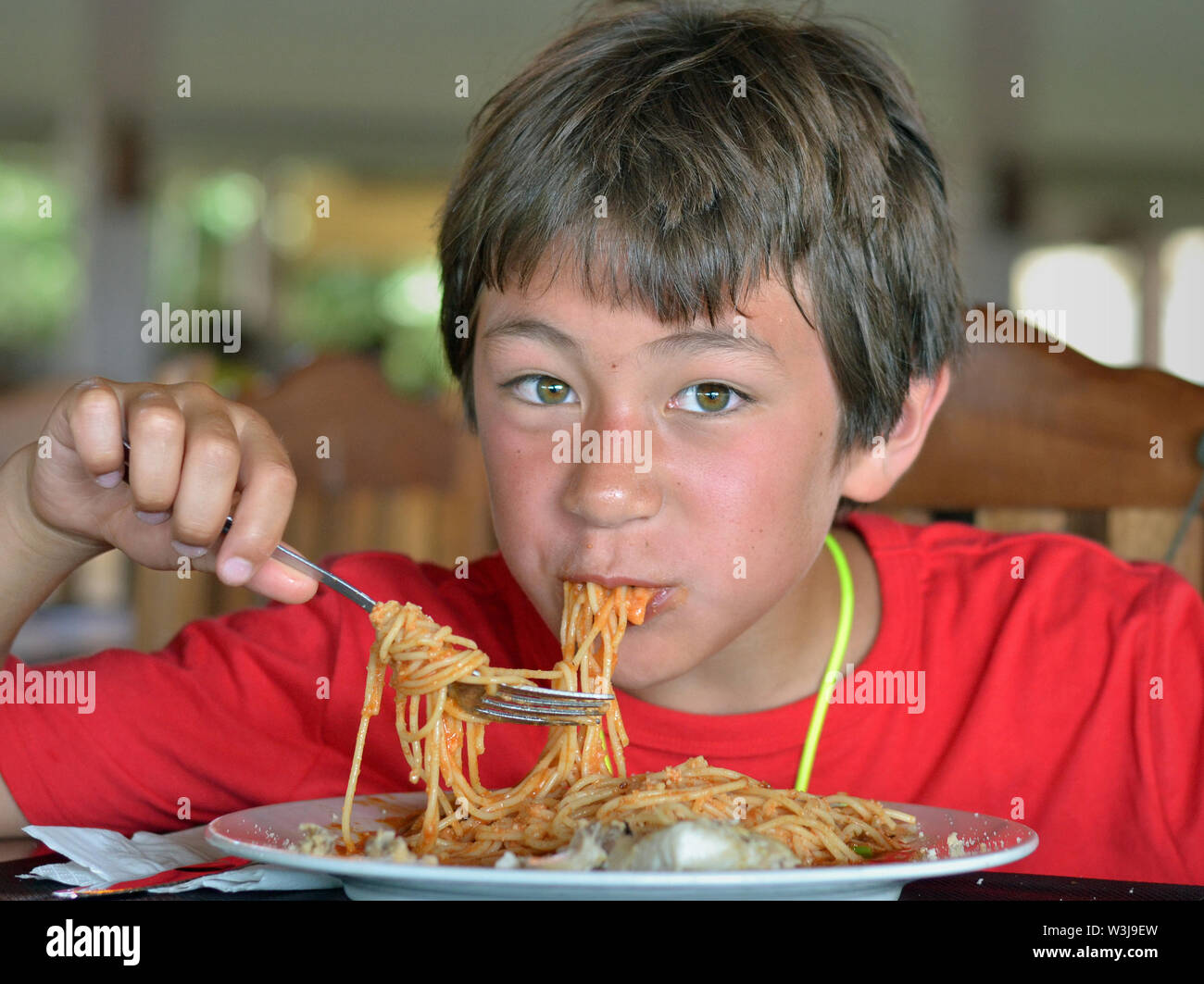 Cute little Canadian boy of mixed-race origin (Caucasian and Southeast Asian) digs into a plate of spaghetti. Stock Photo
