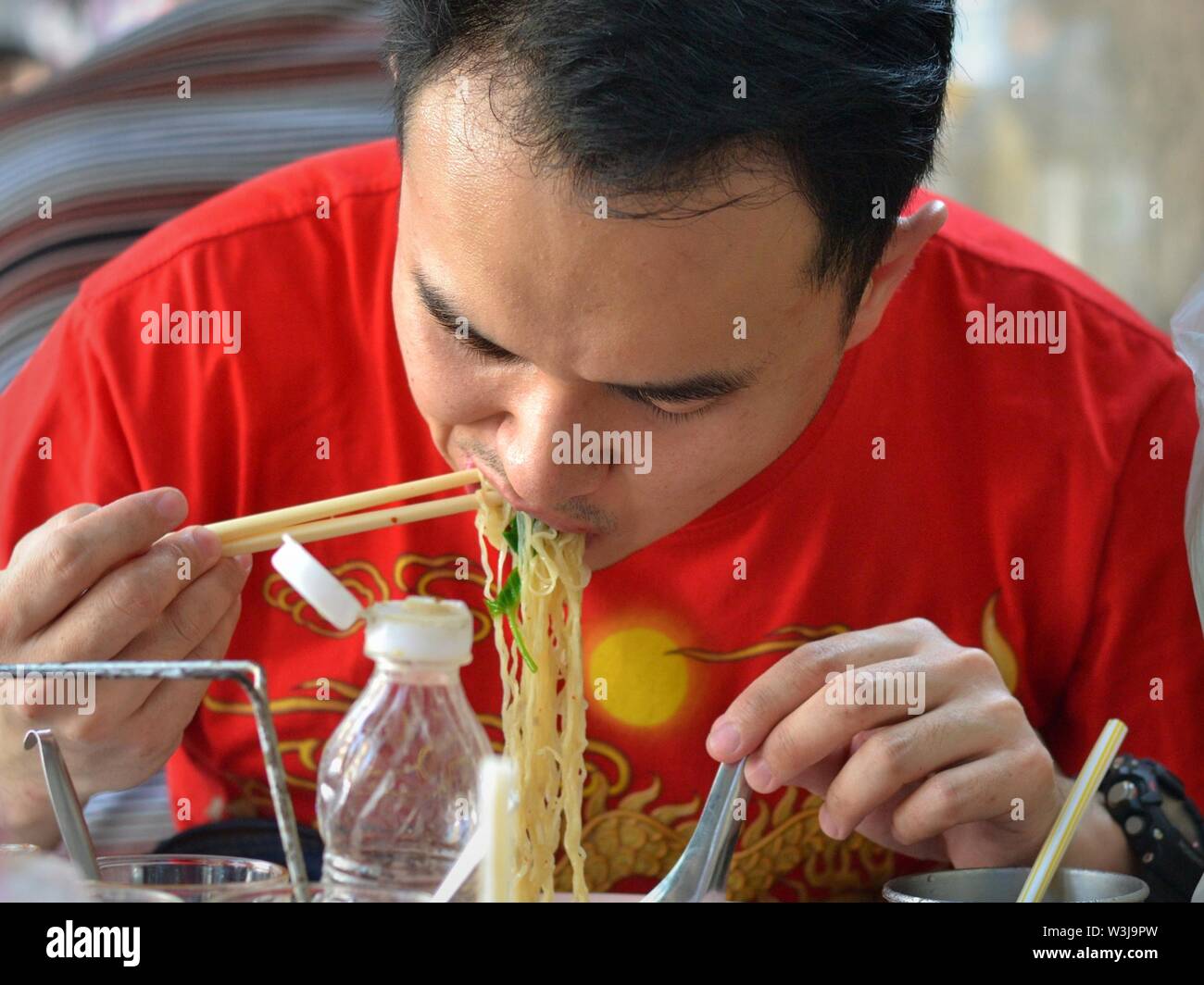 Middle-aged Thai man eats yellow noodles with chopsticks. Stock Photo