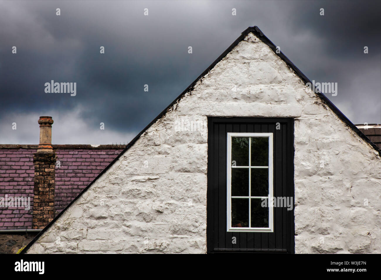 Roof peak on white stone house with window as storm approaches in