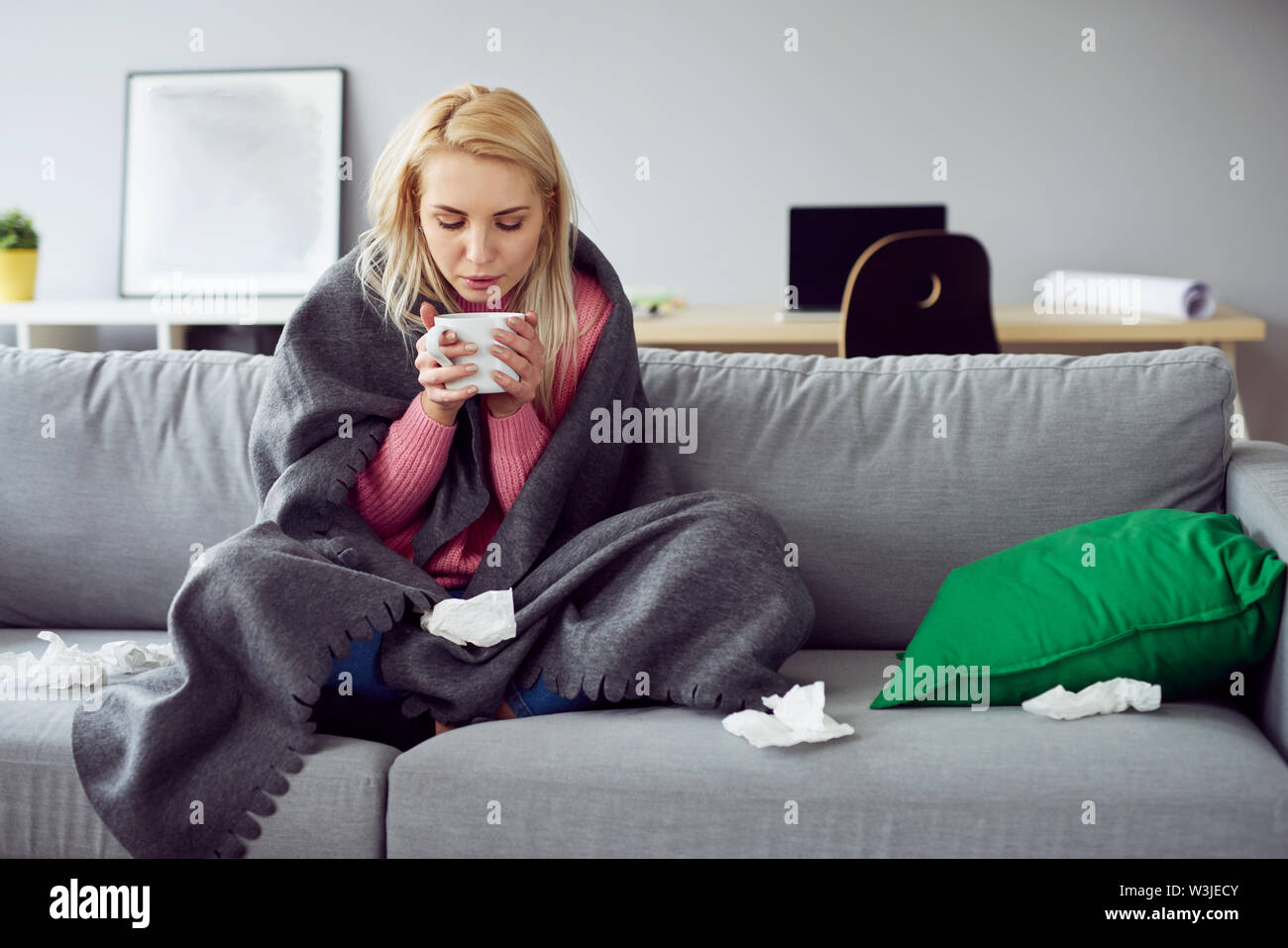 Young sick woman sitting on sofa drinking tea Stock Photo