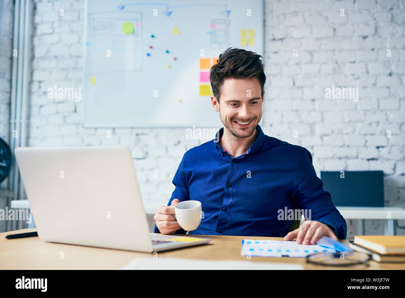 Happy young man working in creative office on laptop looking on documents Stock Photo