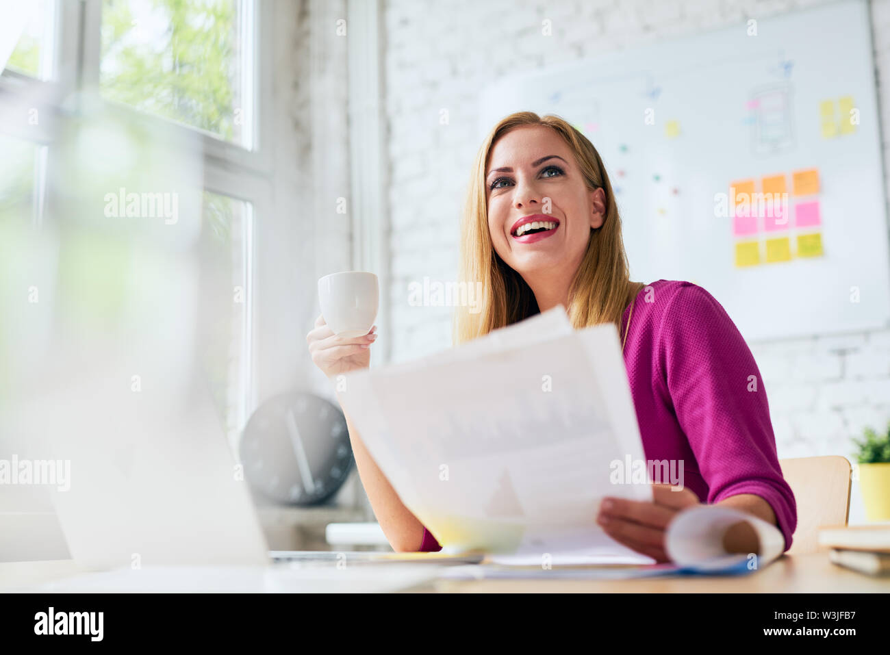 Smiling woman working at office, drinking coffee and browsing documents Stock Photo