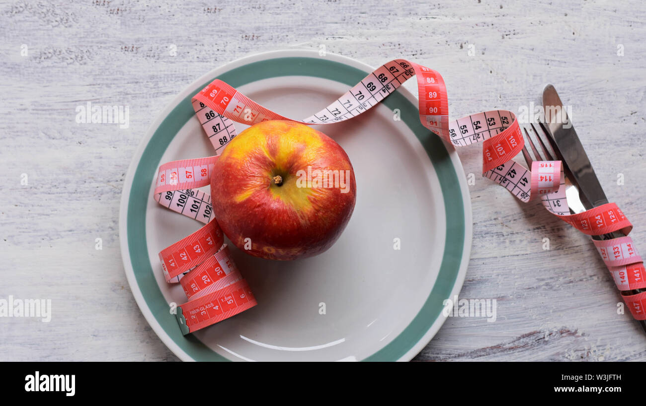 Apple on dish with measure tape, knife and fork. Diet food on wooden table. Weight control - Image Stock Photo