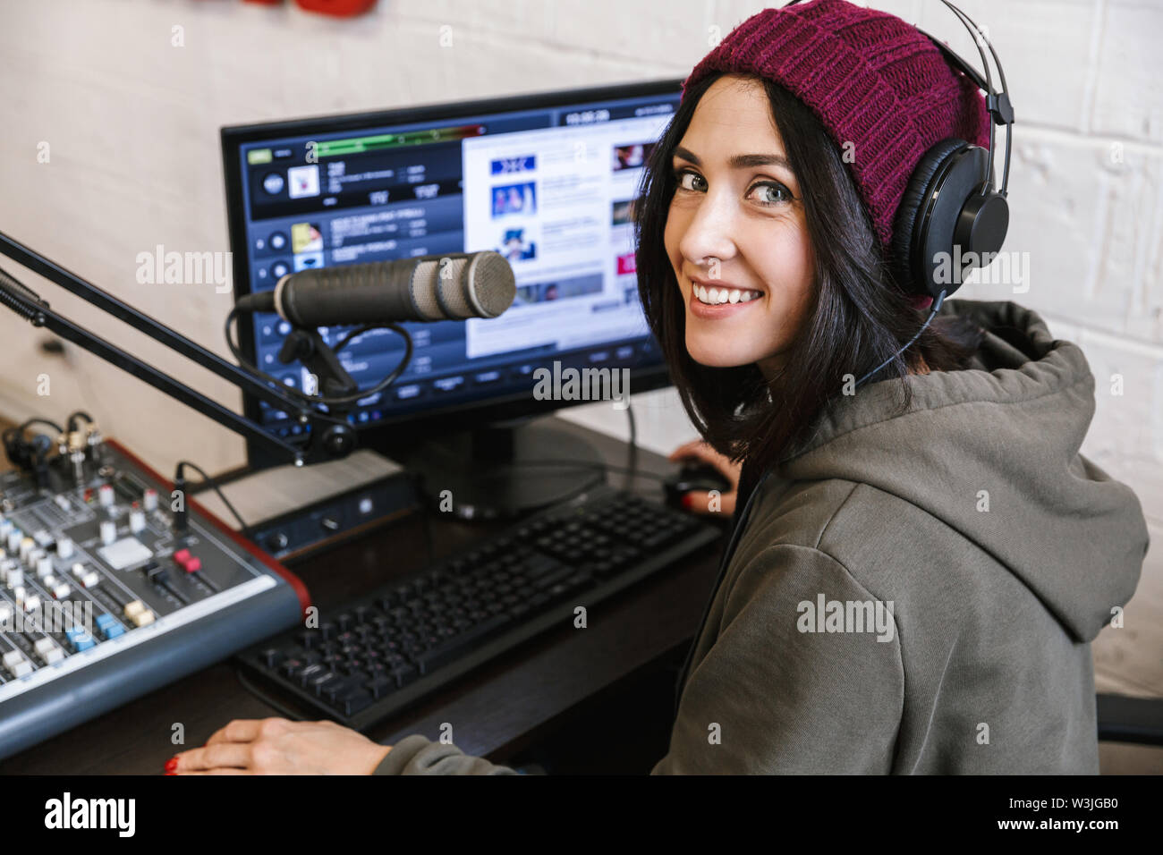 Beautiful happy young female radio host broadcasting in studio, using