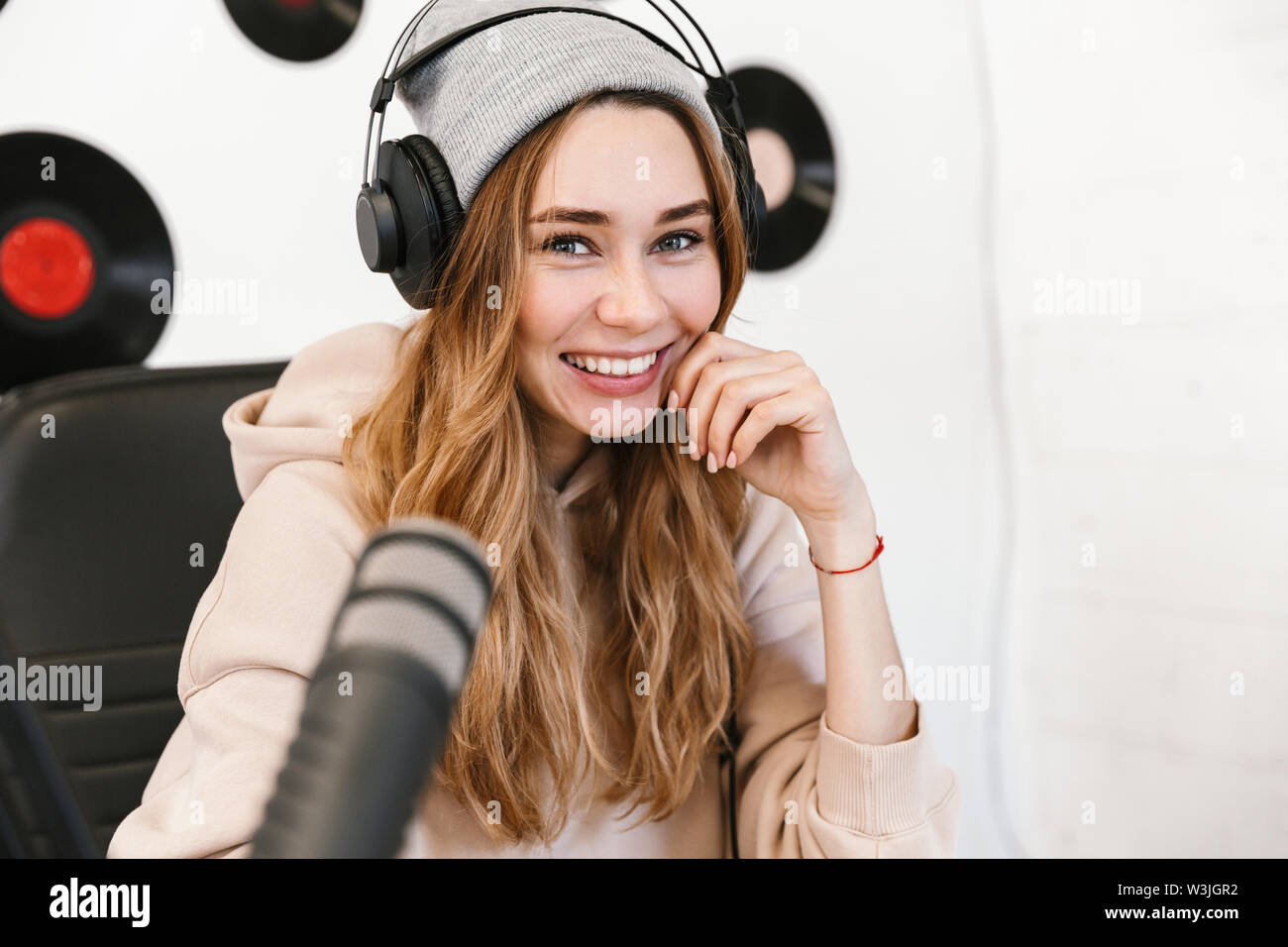Beautiful happy young female radio host broadcasting in studio, using