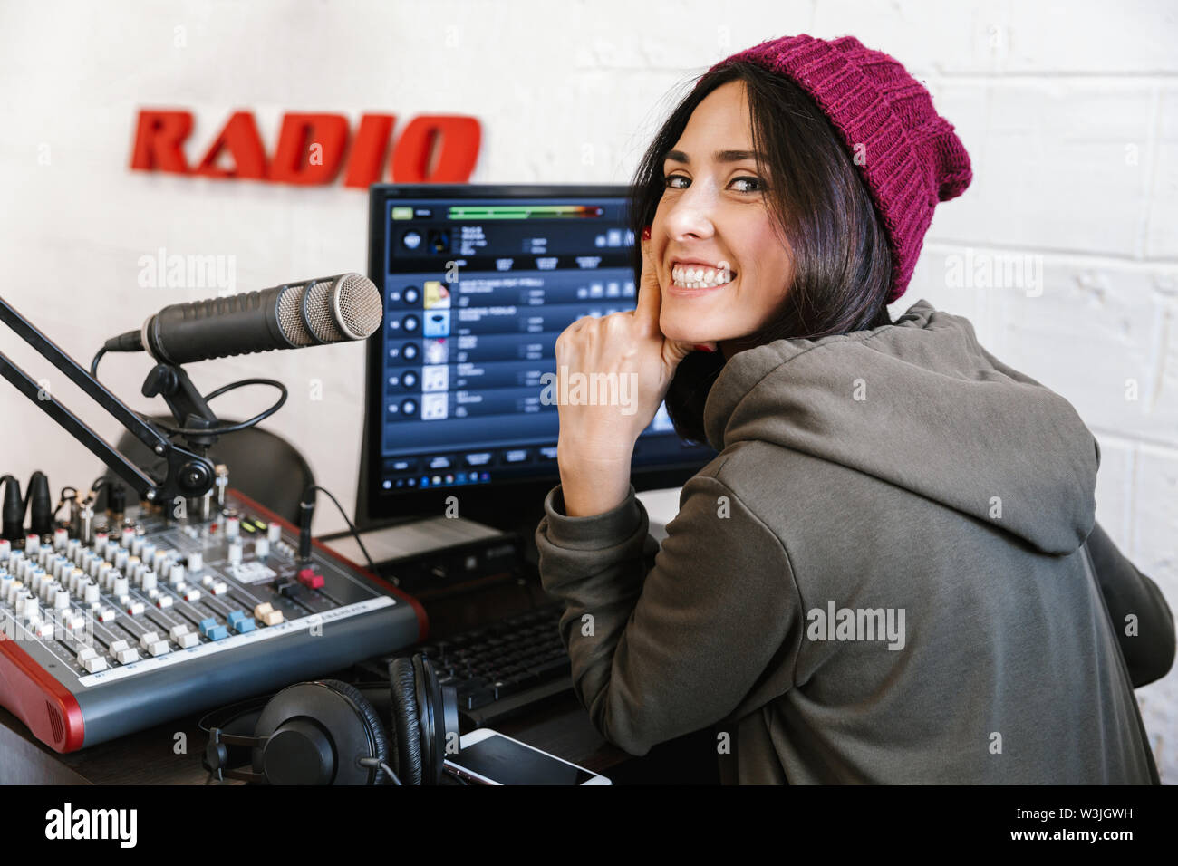 Beautiful happy young female radio host broadcasting in studio, using