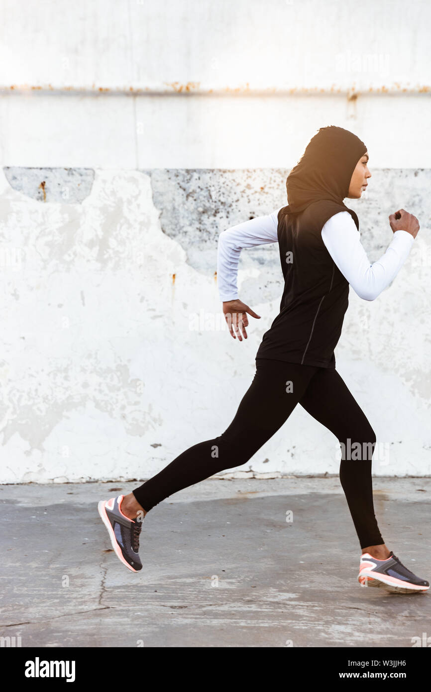 Image of a young concentrated muslim sports fitness woman dressed in hijab  and dark clothes running outdoors Stock Photo - Alamy