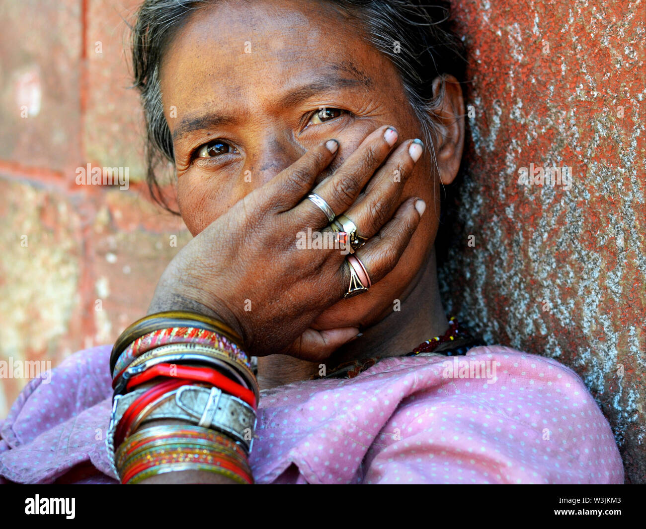 Nepali woman with all-knowing eyes covers her mouth with her left hand (mouth guard gesture) thus showing her bangles and rings. Stock Photo