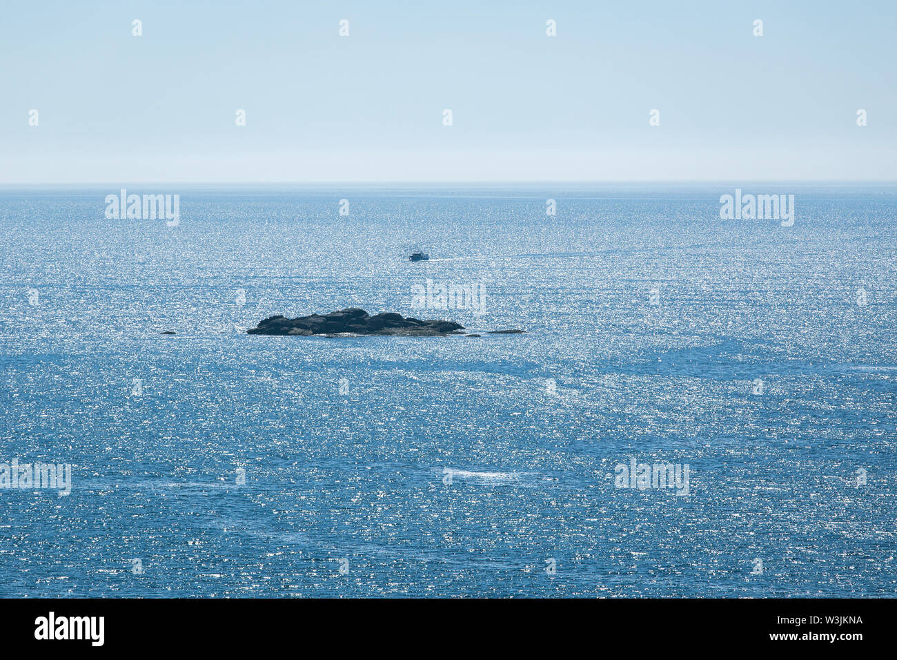 Seascape with a small vessel and a small rock island Stock Photo