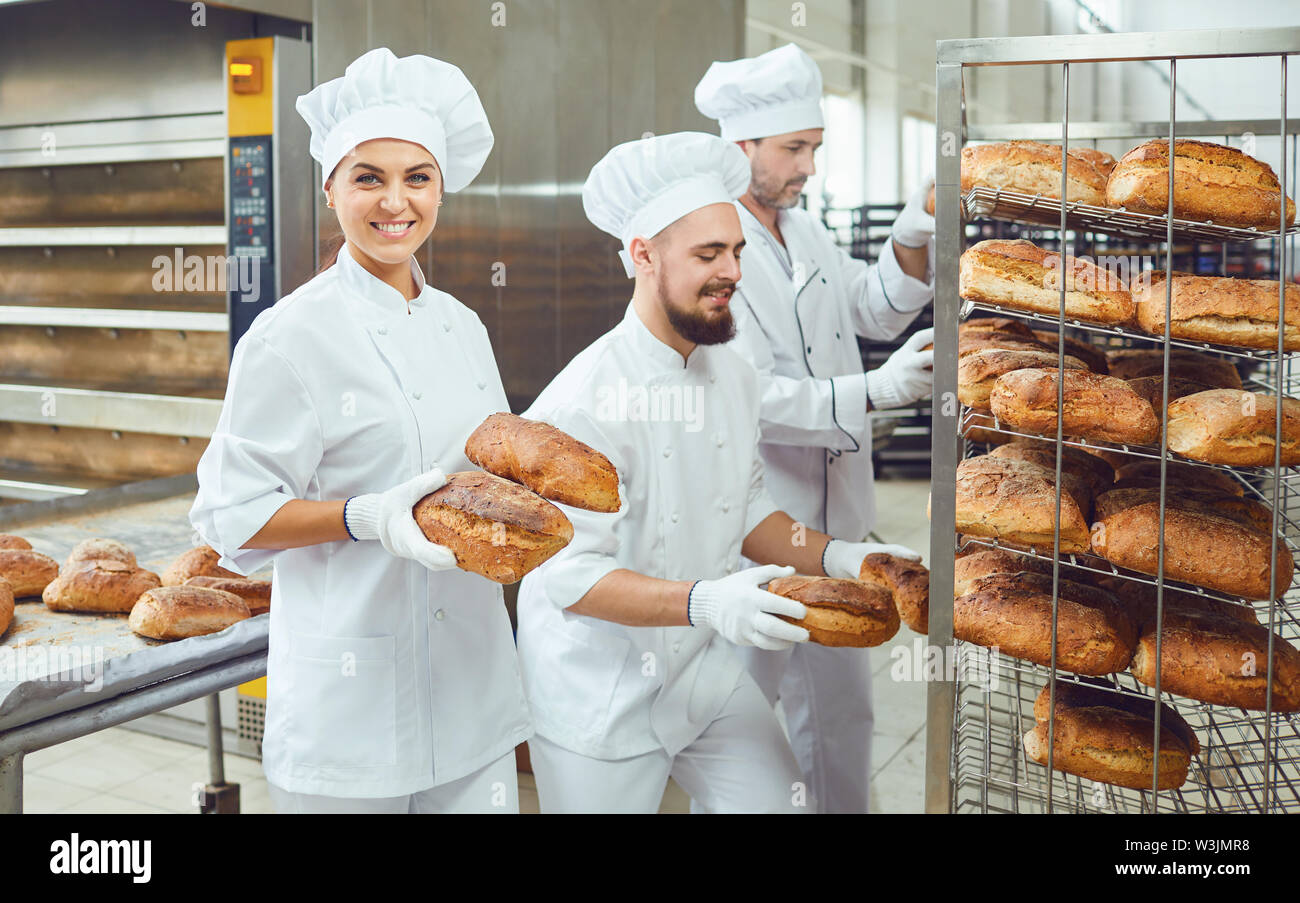A baker woman holds fresh bread in her hand against the background of bakers  working in a bakery Stock Photo - Alamy