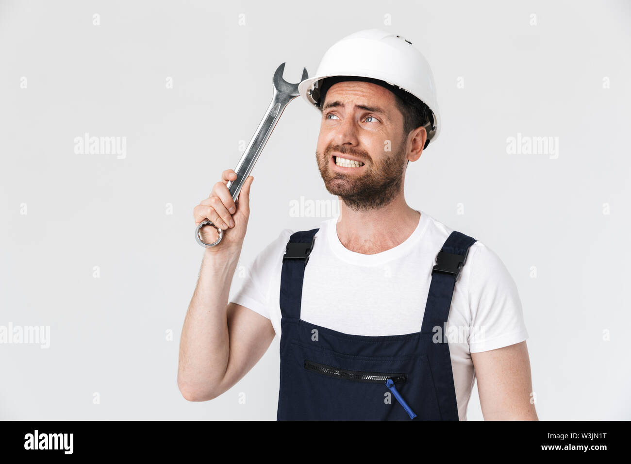 Confused bearded builder man wearing overalls and hardhat standing ...