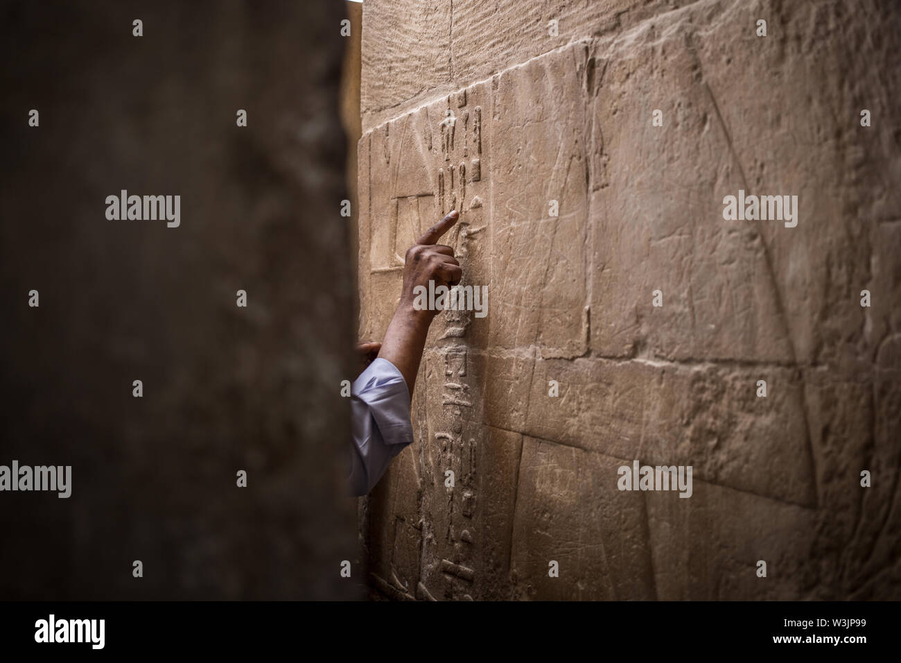 Giza, Egypt. 16th July, 2019. A Egyptian man points at hieroglyphs in the mastaba tomb of Seshem Nefer Theti at the Giza Pyramid complex. Credit: Oliver Weiken/dpa/Alamy Live News Stock Photo