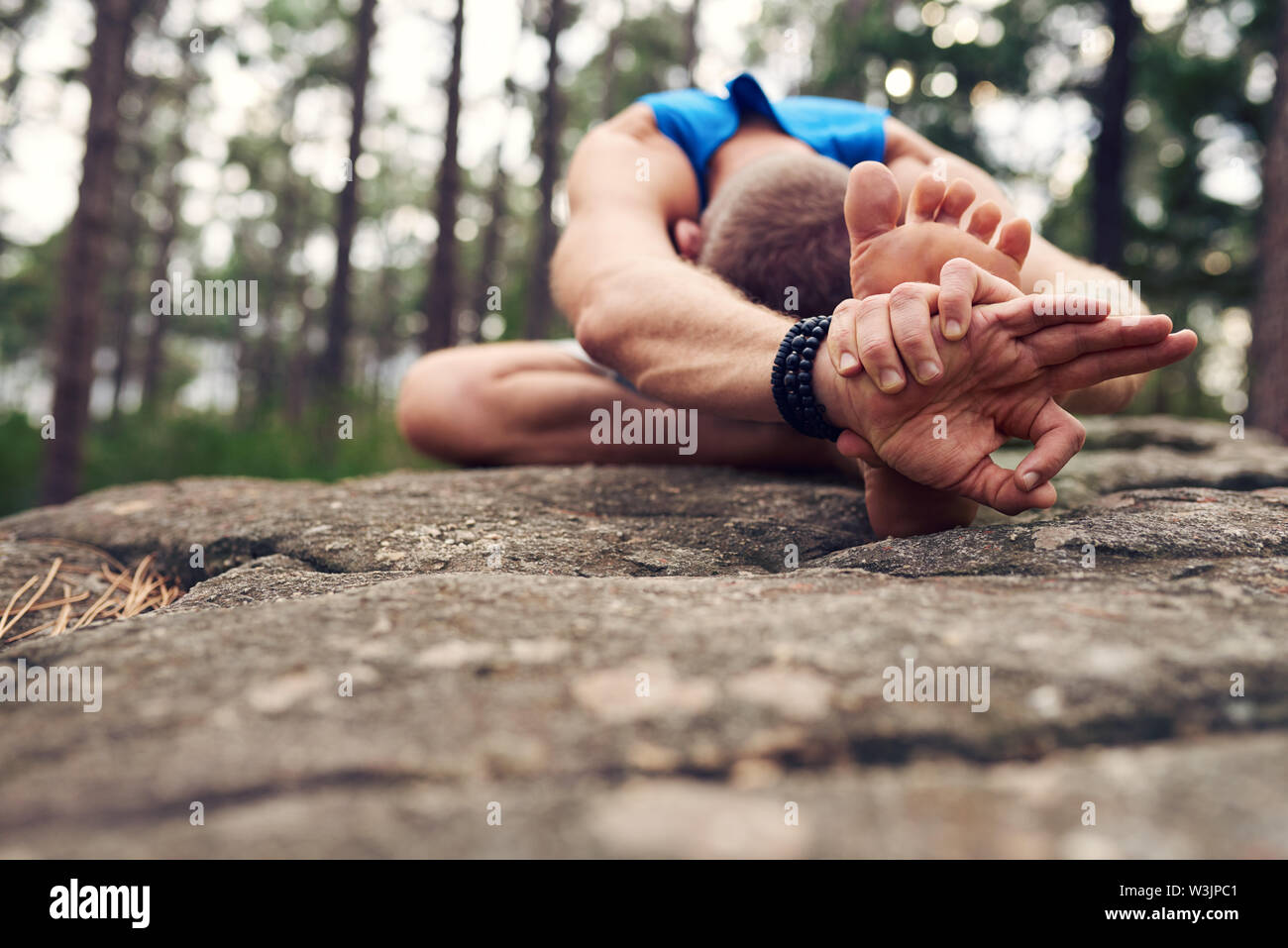 Man doing a head to knee pose in the woods Stock Photo